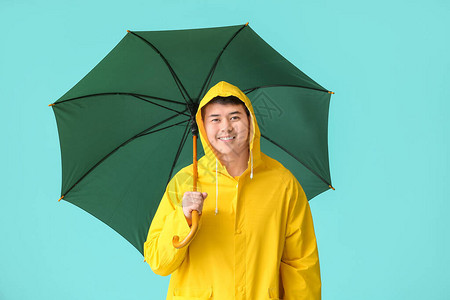 穿着雨衣和彩色背景雨伞的亚洲年轻人图片