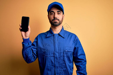 留着胡子身穿蓝色制服头戴帽子的机械师手持智能手机屏幕图片