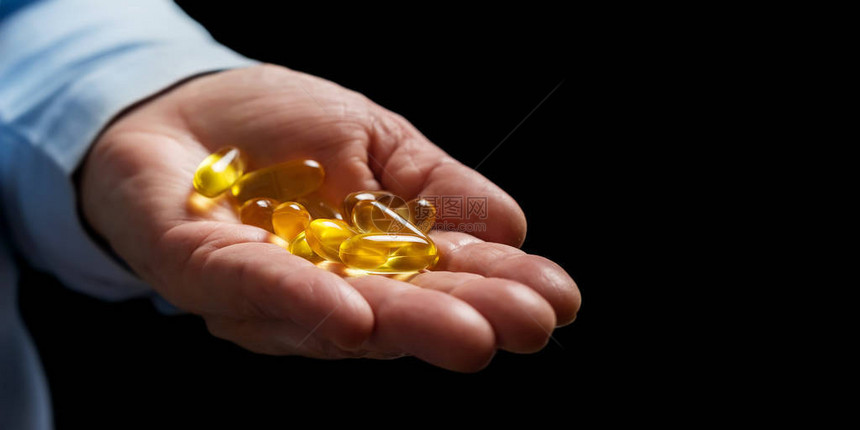 乳黄3鱼油和健康补充药丸的胶囊在黑底棕榈手的女人身上图片