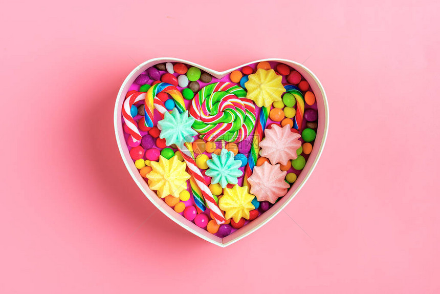 混合的多彩巧克力糖放在心形的礼物盒里在色彩丰富背景上平图片
