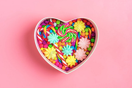混合的多彩巧克力糖放在心形的礼物盒里在色彩丰富背景上平图片