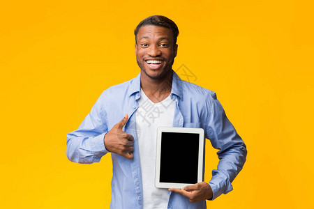 欢欣鼓舞的非洲男子展示空板屏幕在黄色背景上站立的相机上闪烁缩略图图片