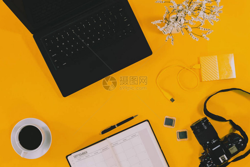 概念工作区笔记本电脑和咖啡杯带相机的笔记本和白花瓶带有USB的外部硬盘在柔和的背景黄色上顶视图图片