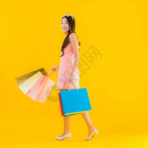 从百货店和购物商场以黄色孤立背景购买多彩购物袋的美丽年轻亚洲妇女肖像般美背景图片