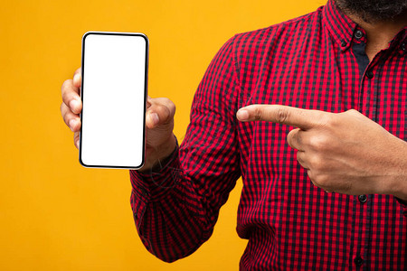 一个面目全非的洲裔美国人手持白色空白屏幕的智能手机并指着它的特写图片