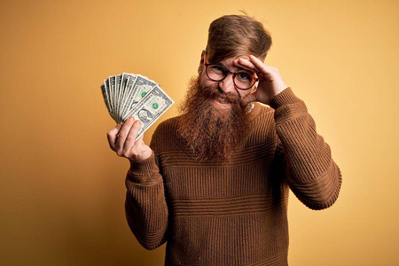 留着胡子的爱尔兰红发男子拿着一堆1美元钞票在黄色背景上图片