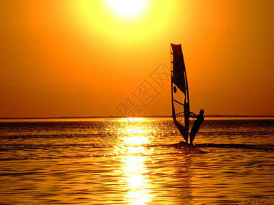 风帆冲浪者在日落海湾的波浪上的剪影背景图片