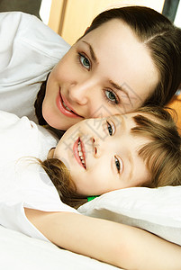 美丽的年轻母亲和小女儿在床上在图片