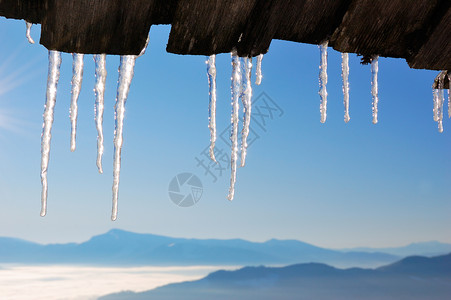 那些从木屋顶上悬在蓝天和山顶的冰柱上图片