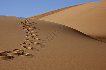 蓝天沙漠丘上的脚印图片