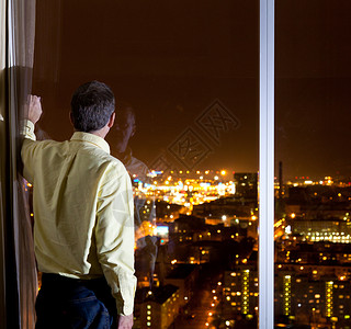 中年男子从酒店或办公室的高窗口向城市外望图片