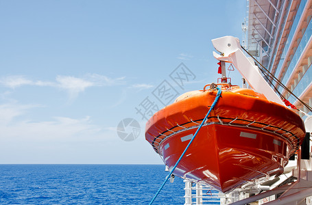 一艘橙色救生艇悬挂在游轮一侧的蓝色大海上图片