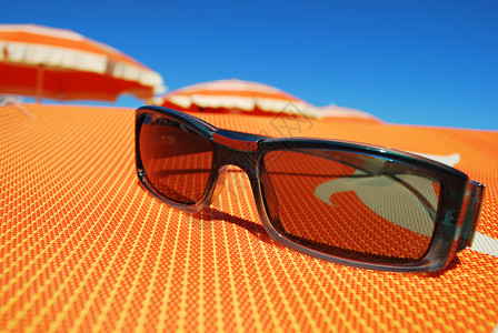 太阳镜和海滩橙色带条纹雨伞和蓝天背景图片