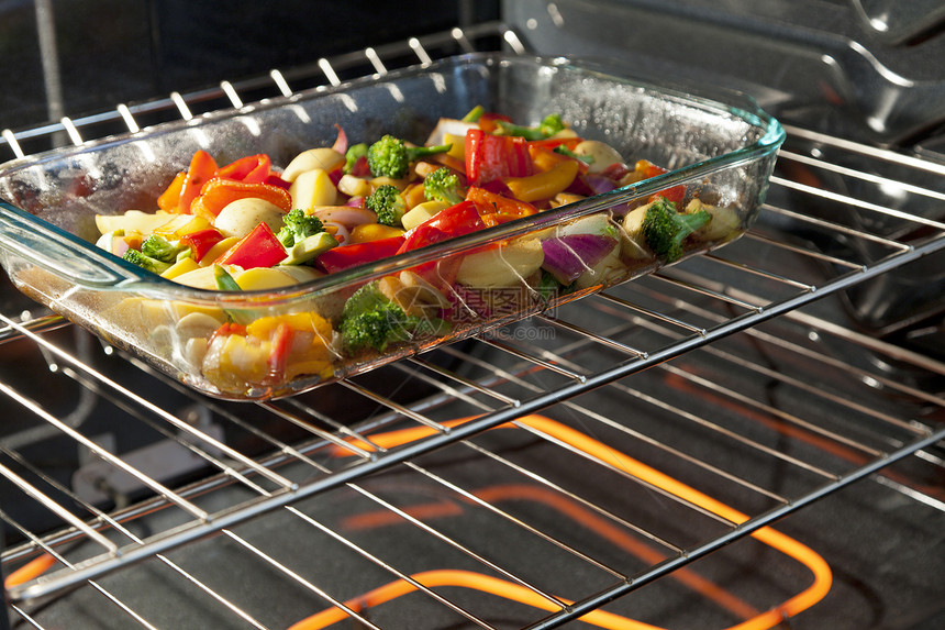 新鲜蔬菜在烤箱中的透明盘中烘烤图片