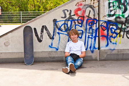 男孩在滑板公园里拿着滑板休息图片