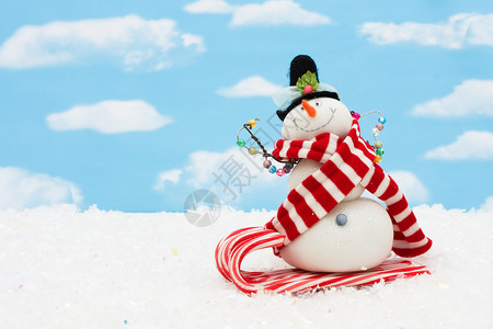 雪人坐在甘蔗雪橇上的雪人在蓝天背景上图片