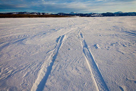 在冰冻湖表面的深雪中滑雪在车胎足迹上直至阳图片