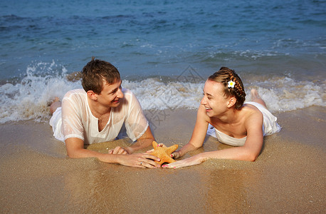 与泰国普吉岛的海星一起在晚沙滩上躺在白棉衣服上的年轻图片
