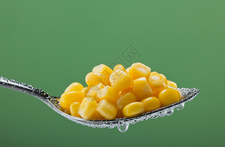 绿色背景金属勺中保存玉米蔬菜的宏观照片以图片