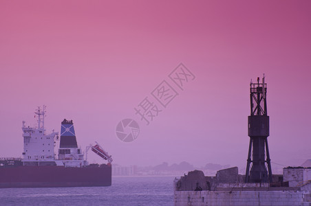 带有灯塔和货船的戏剧粉红色日落图片
