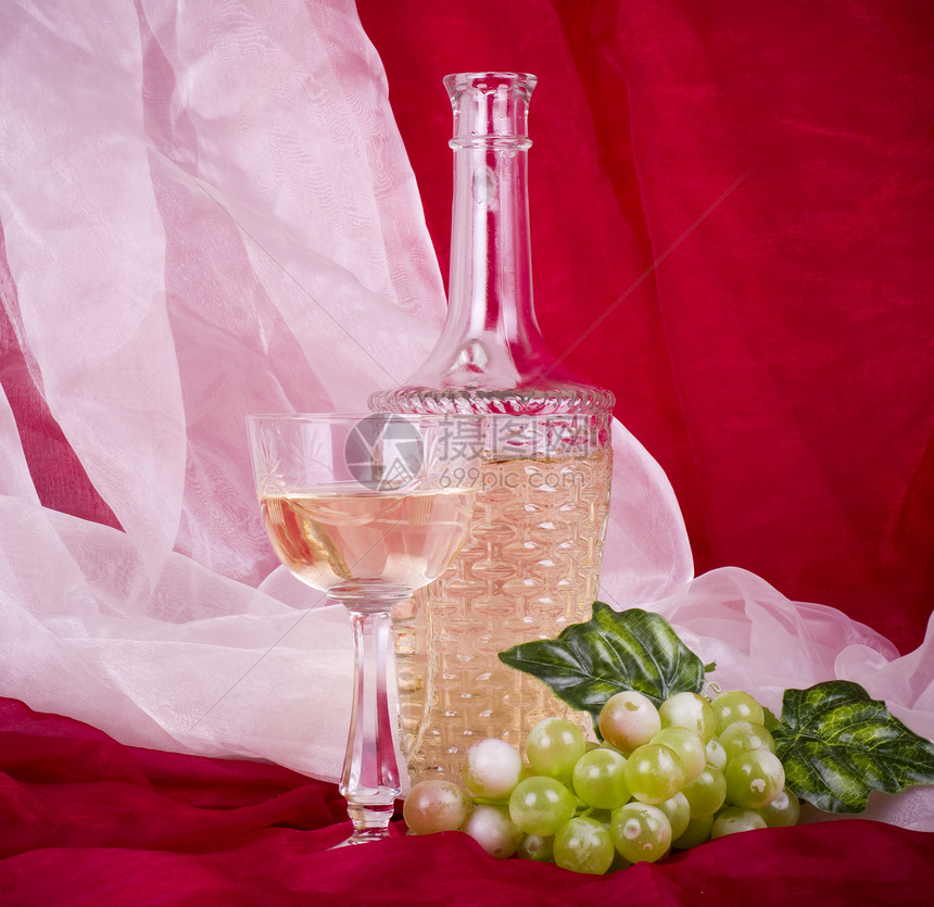 红色背景中带绿葡萄的玻璃瓶酒图片