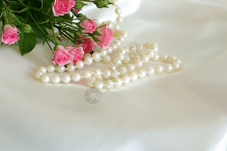 白色丝绸上的玫瑰和珍珠图片