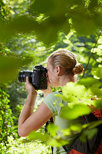 年轻女子在树间徒步旅行并用单反相机拍照图片