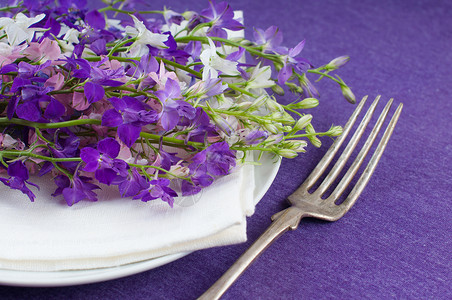 紫色背景中的节日餐桌布置盘子叉子和一束鲜花图片