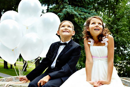 儿童新娘和新郎的肖像与坐在公园里的气球图片