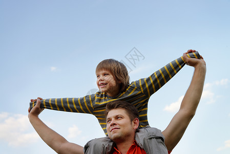 父亲的肩膀上是快乐的儿子在蓝天的图片