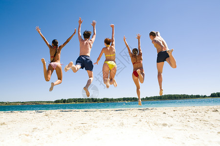 快乐的朋友在沙滩上跳跃的背影图片