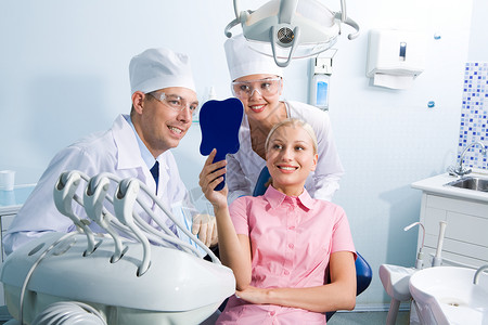 女青年在牙医和助理的包围下用镜像照图片