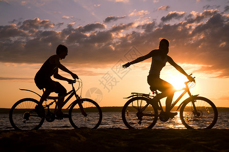 日落时快乐情侣骑自行车在海岸骑自图片