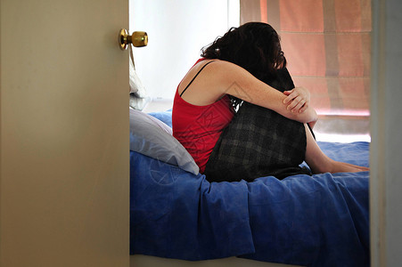 坐在家中卧床上的情绪压抑的年轻女患高清图片