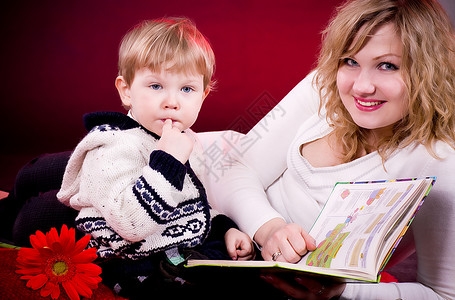 母亲和婴儿男孩阅读书在红图片