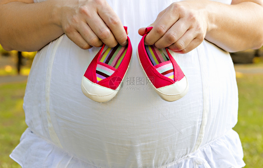 怀孕的母亲拿着粉红色的婴儿鞋图片