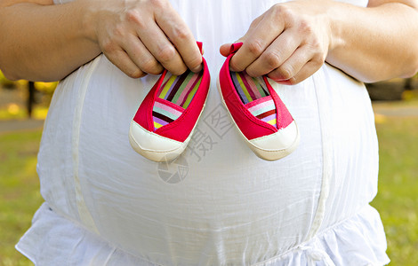 怀孕的母亲拿着粉红色的婴儿鞋图片
