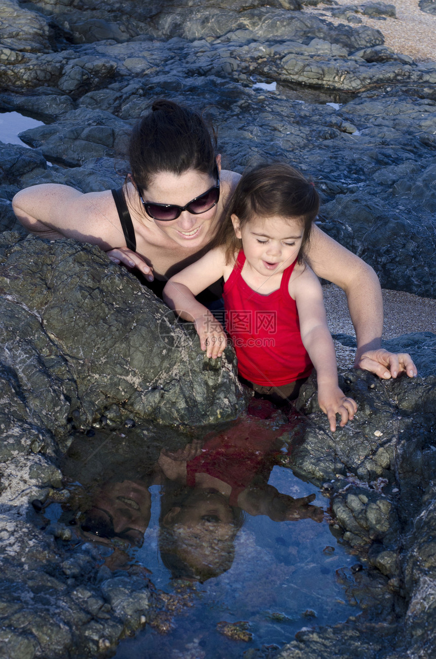 一个年轻的母亲和她幸福的女儿看着海边岩石中的水面板图片