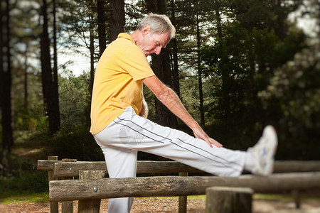 老人在伸展腿部自然锻炼健康生活森林户外黄衬衫和白裤图片