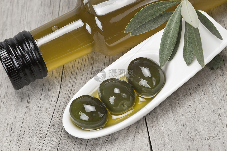橄榄油瓶和一些橄榄在木质表面图片