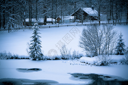 雪地阿尔卑斯山的房子和森林中的冰冻河流图片