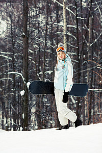年轻美女拿着雪板在滑雪坡上行走图片