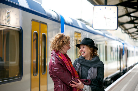两个成熟的女朋友在户外火车站平台上微笑和热情拥抱地相互欢迎图片
