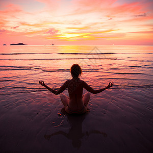 日落时在海边沙滩上的瑜伽女人图片