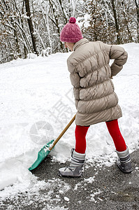 年轻女子用绿色铲子在街上铲雪图片