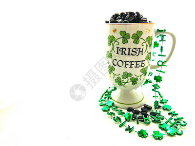 爱尔兰咖啡杯与棕色咖啡豆和绿色三叶草在圣帕特里克节的孤图片