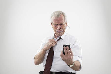英俊的老年男子放松他的领带反应令人厌恶并不喜欢来电话或短信在手机上拉图片