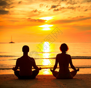一对年轻夫妇坐在海边的沙滩上日落时分在莲花的位图片