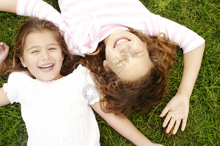 两个女孩躺在绿草地上笑着倒在地图片