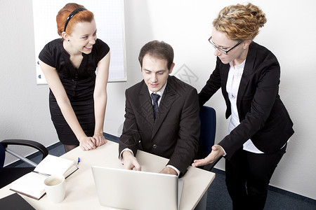 一男两女成功微笑的商业团队聚集在办公室的笔记本电脑旁图片